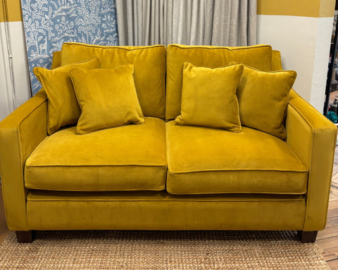 Yellow sofa with decorative pillows against a yellow wall with floral and plain curtains.